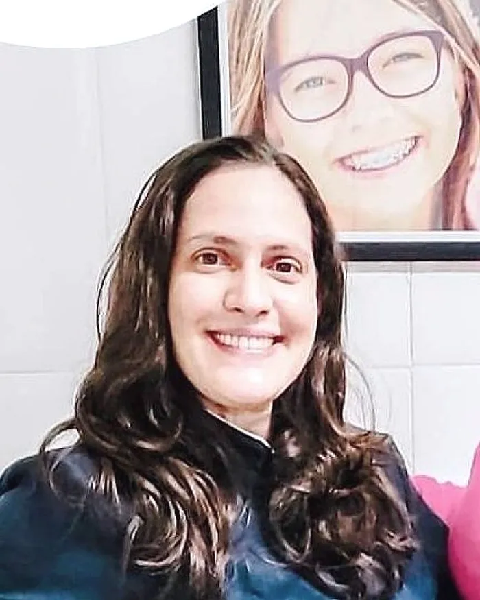 Dra. Clariana sorrindo, de blusa azul-marinho, no consultório
