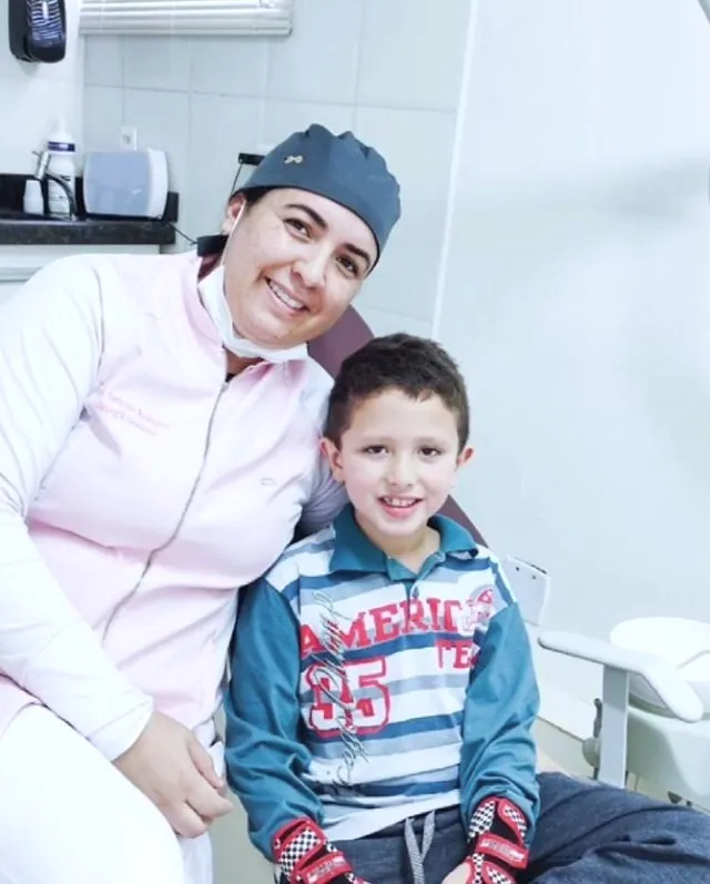 Dra. Andressa sorrindo ao lado de um menino na cadeira do consultório